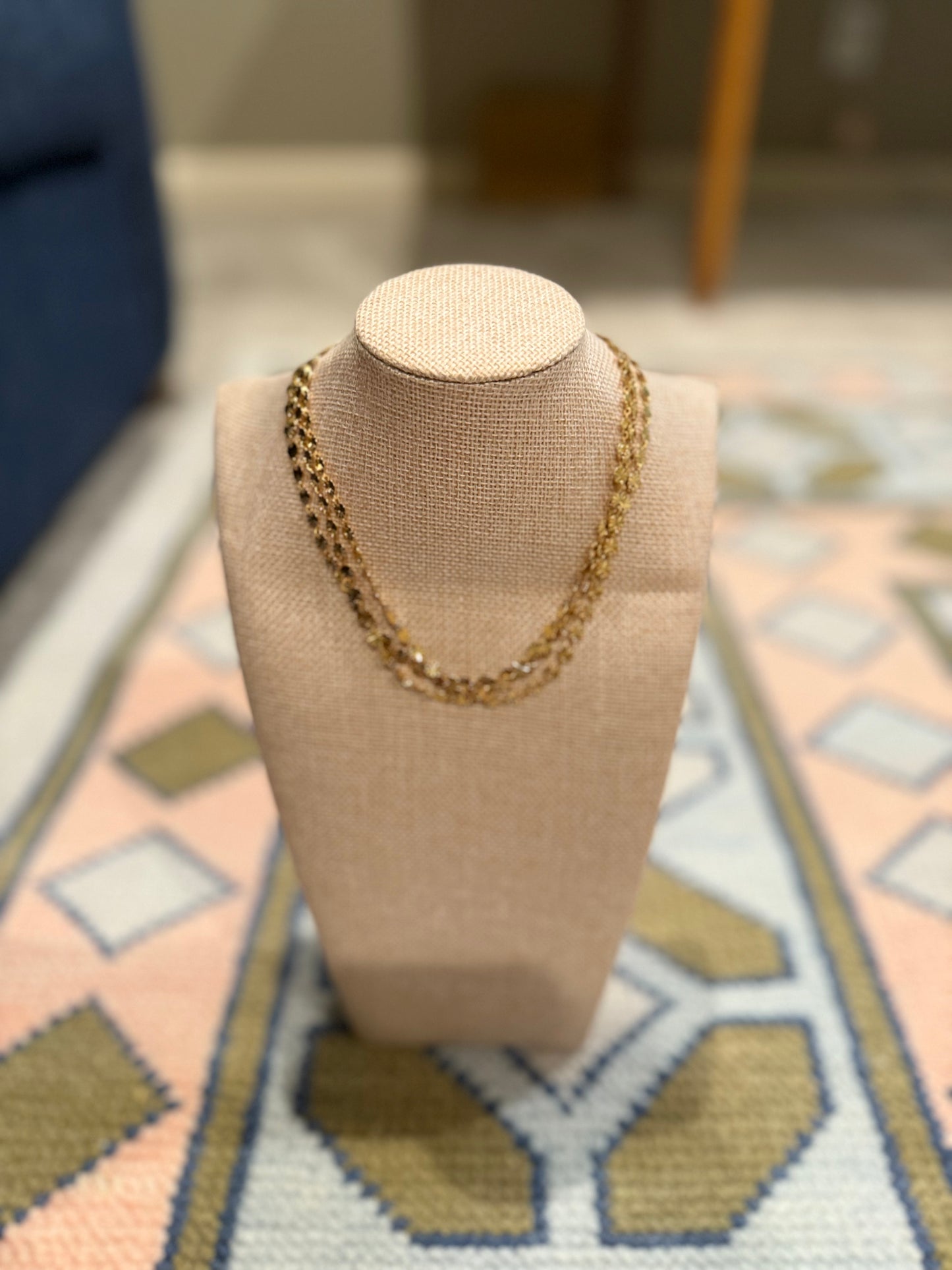 Gold chain necklace on a beige mannequin bust against a patterned rug.
