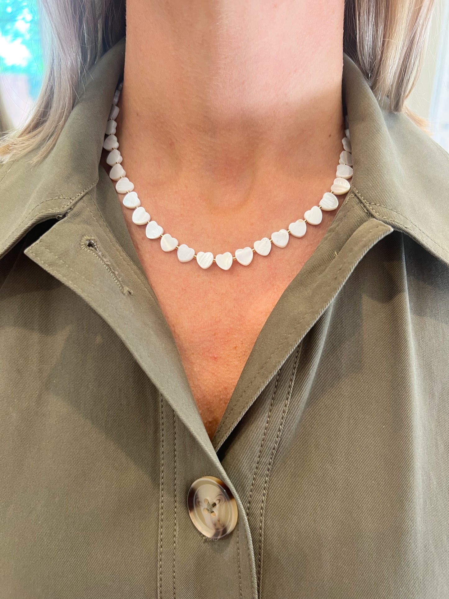 Person wearing a green jacket with a heart-shaped necklace