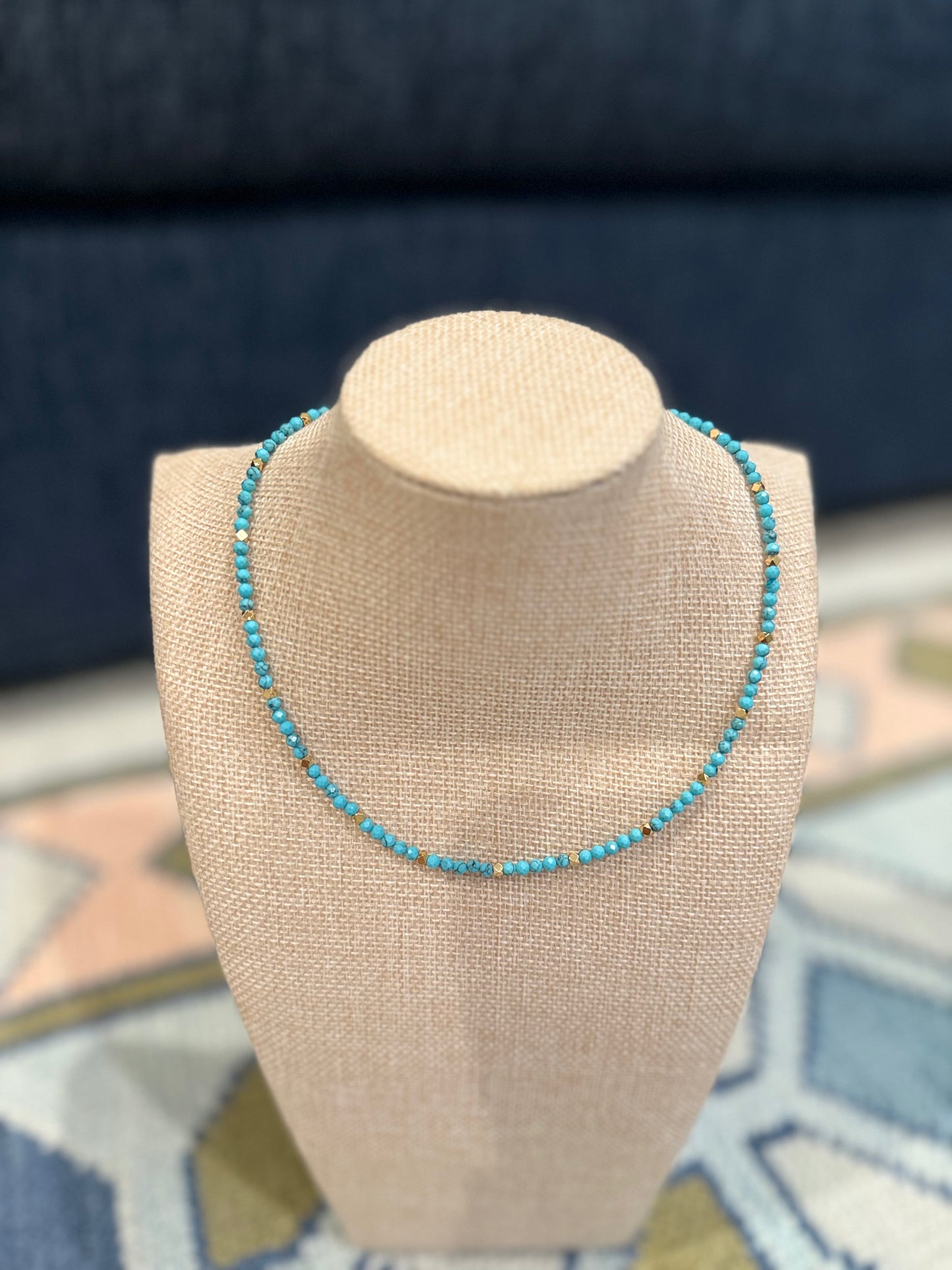 Turquoise beaded necklace on a beige mannequin bust with a blue fabric background