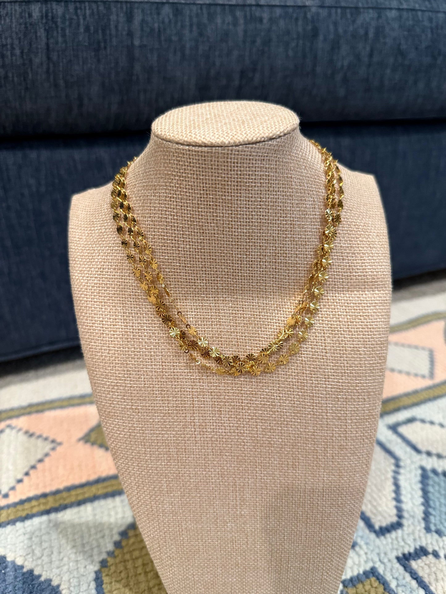 Gold necklace on a beige mannequin bust with a blue textured background