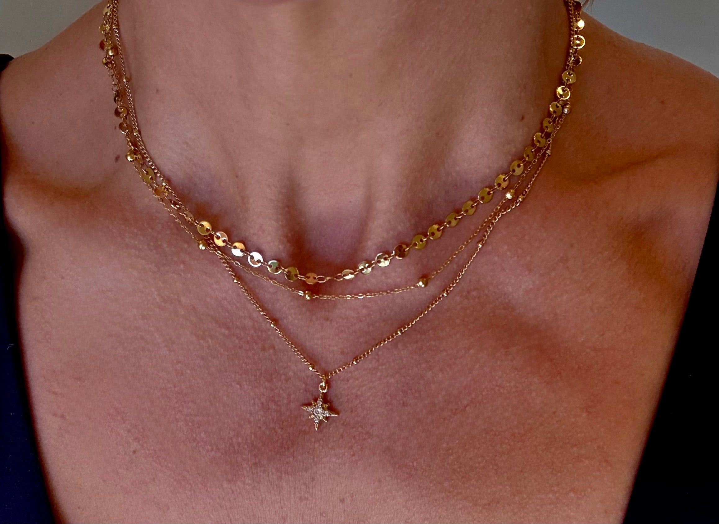 Close-up of a person wearing two gold necklaces with a star pendant.